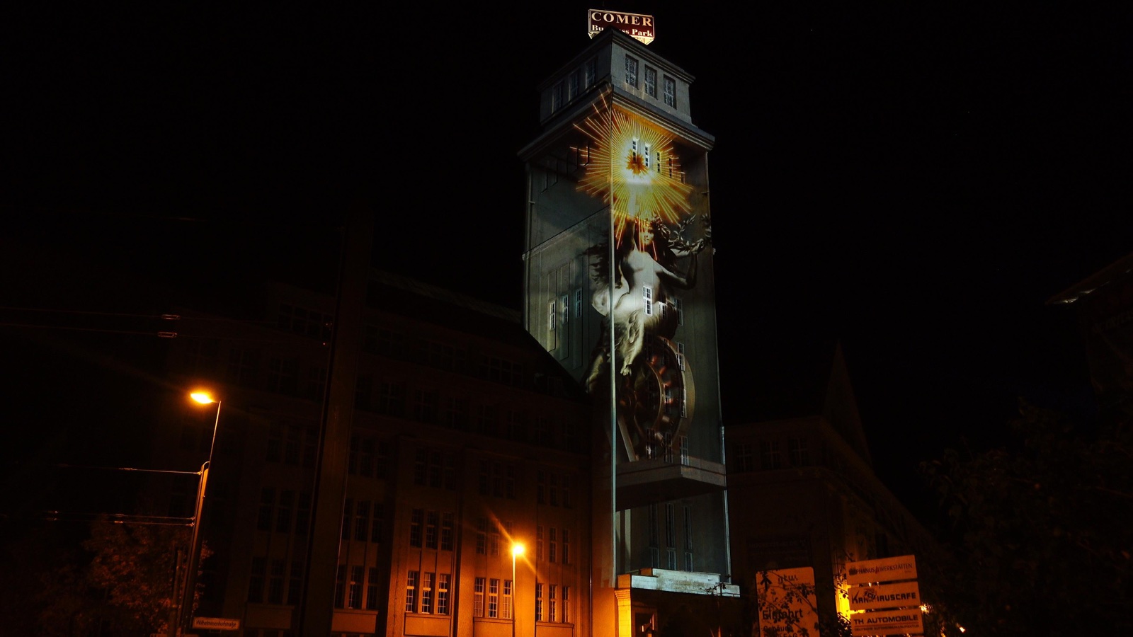 The tower of the Peter Behrens Bau in Berlin under a projection mapping for 100 Years of E-Mobility, filmed from the street at night