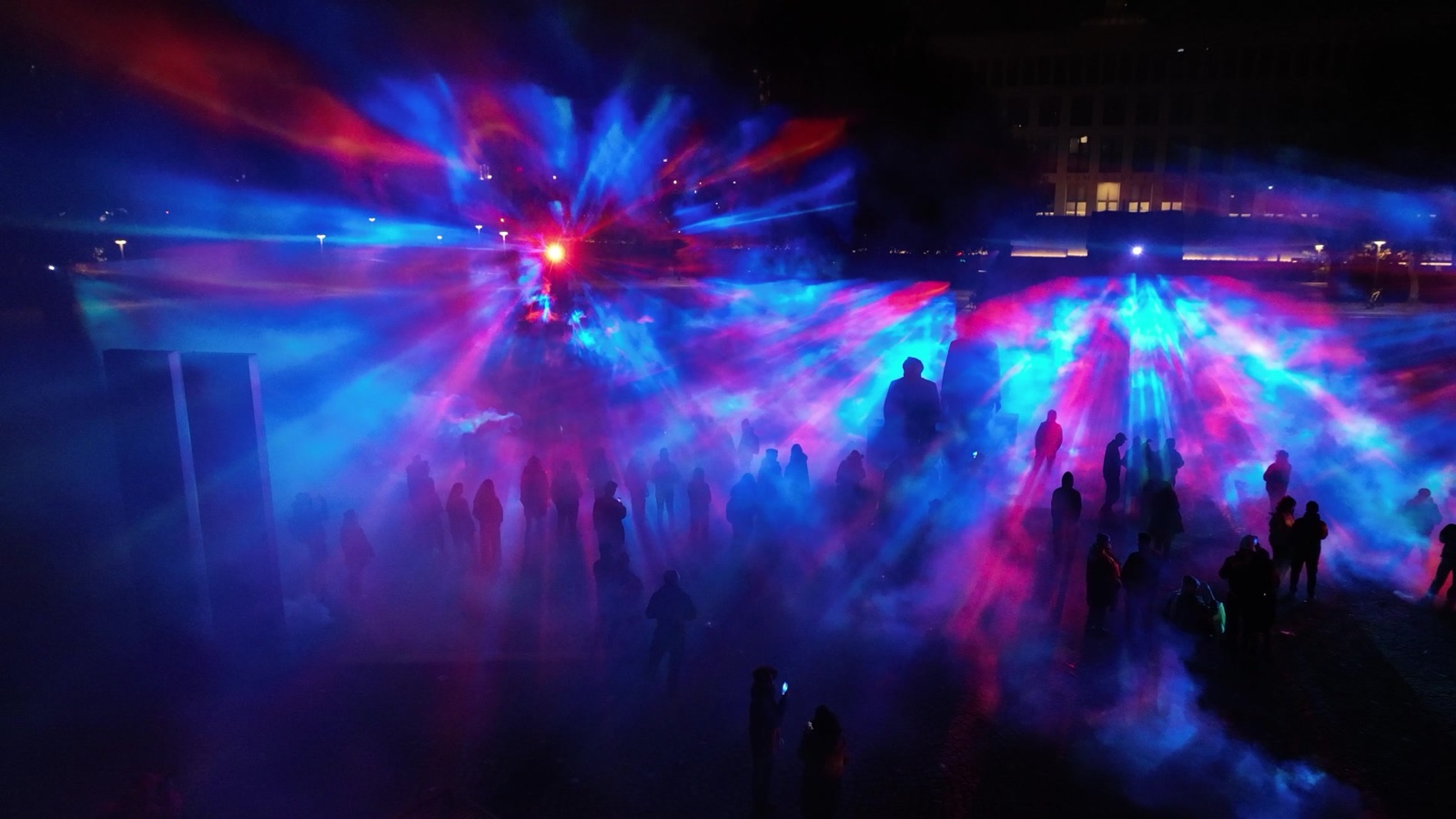 Visitors standing inside ÆTHER, a walk-in installation of green, magenta and blue light beams in fog at the Marx-Engels-Forum in Berlin
