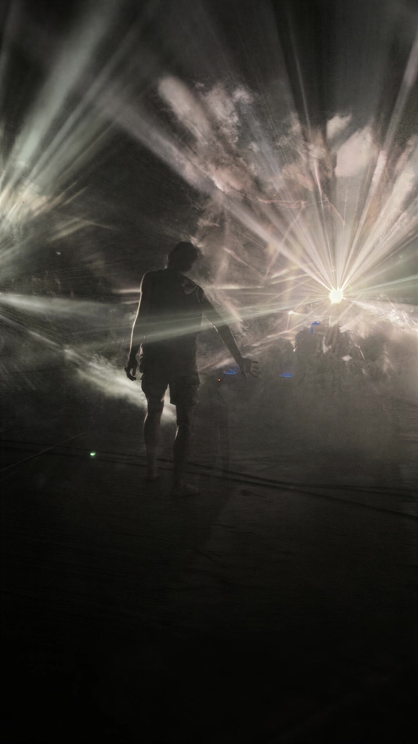 A visitor stands as a silhouette inside BEYOND at MaHalla Berlin, surrounded by radiating beams and clouds of light in fog