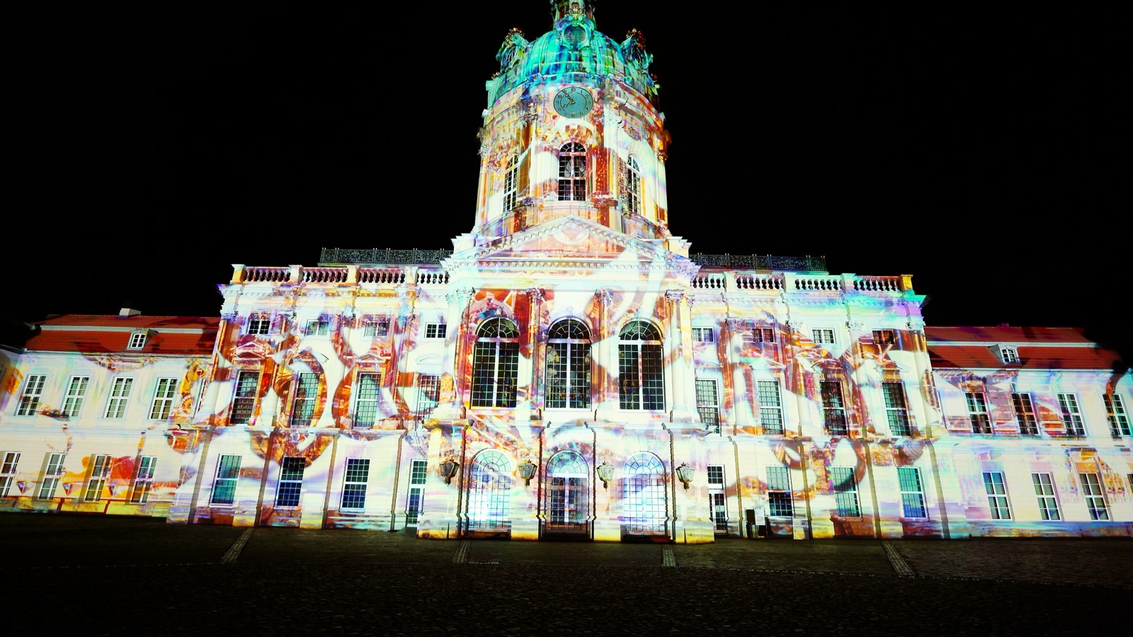 The façade of Charlottenburg Palace in Berlin lit white, with red and orange ribbons of projected light coiling across it during the Festival of Lights 2022