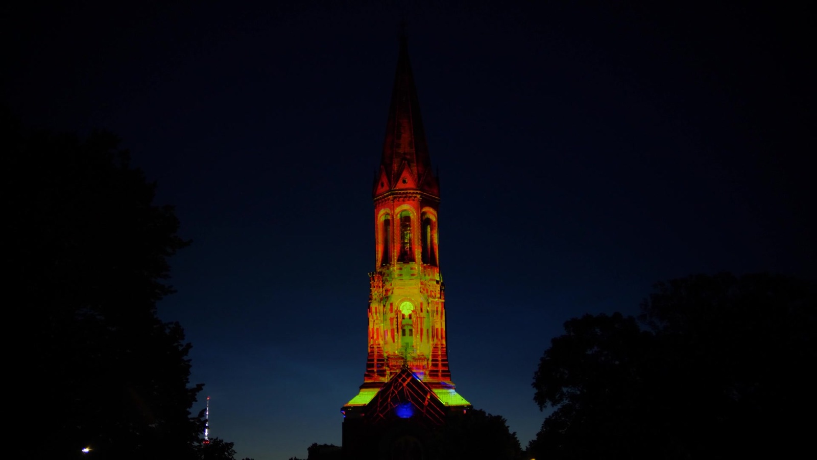 The Emmauskirche tower in orange and yellow light from the projection, against a dark blue sky