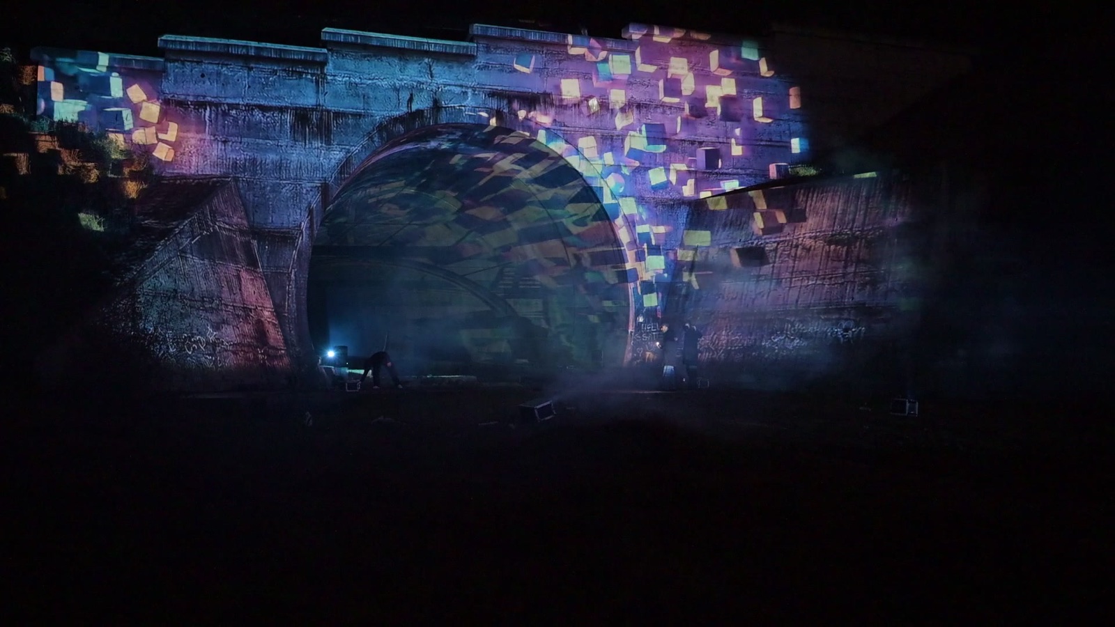 A railway tunnel portal in Tbilisi covered in a projection mapping of coloured tiles, with a hologram of light appearing in the tunnel mouth