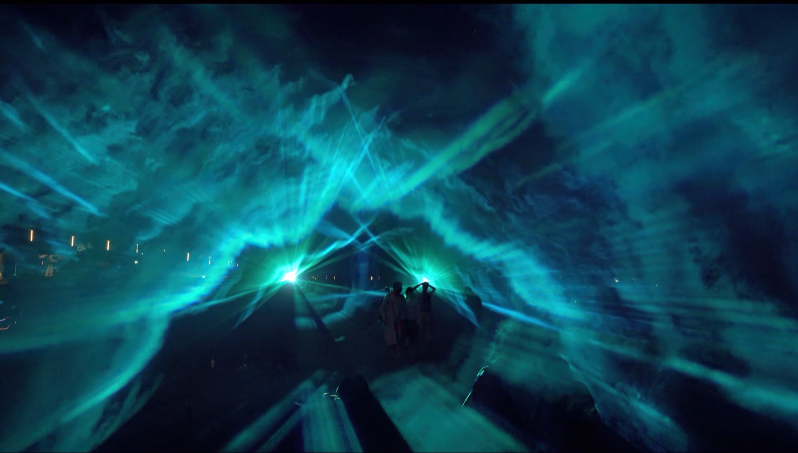 Turquoise beams spreading across the night in a wide fan above the crowd