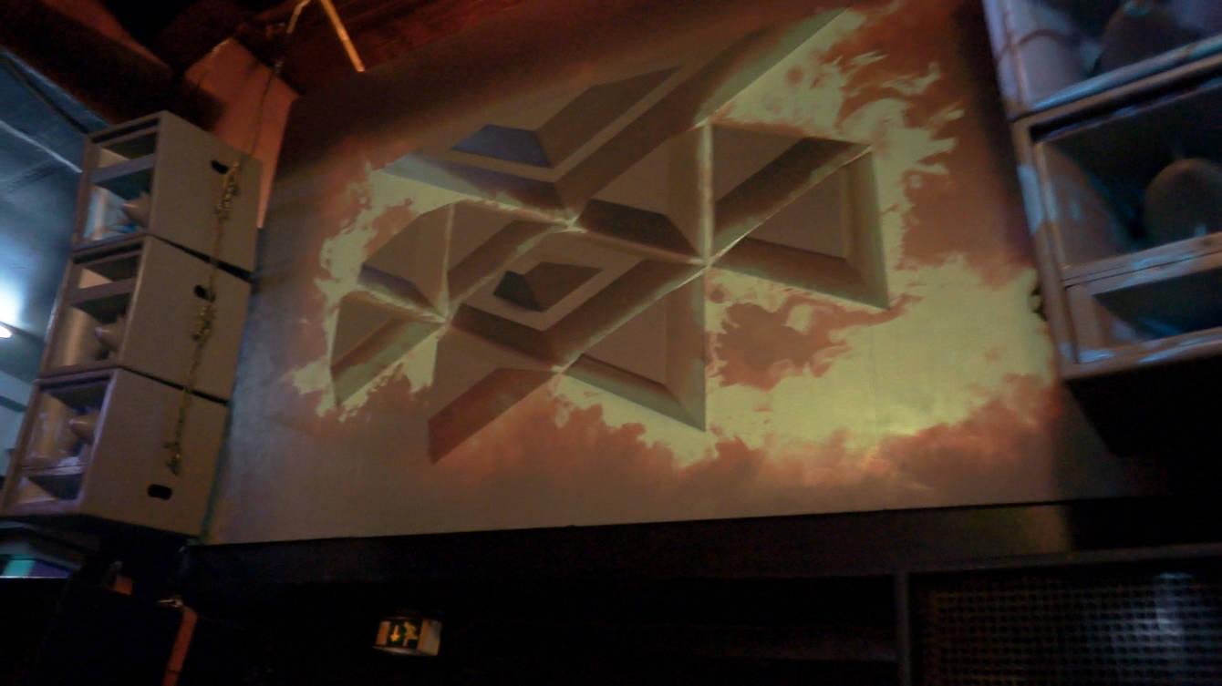 A geometric stage structure inside the Juice Club Hamburg lit by projection-mapped animations
