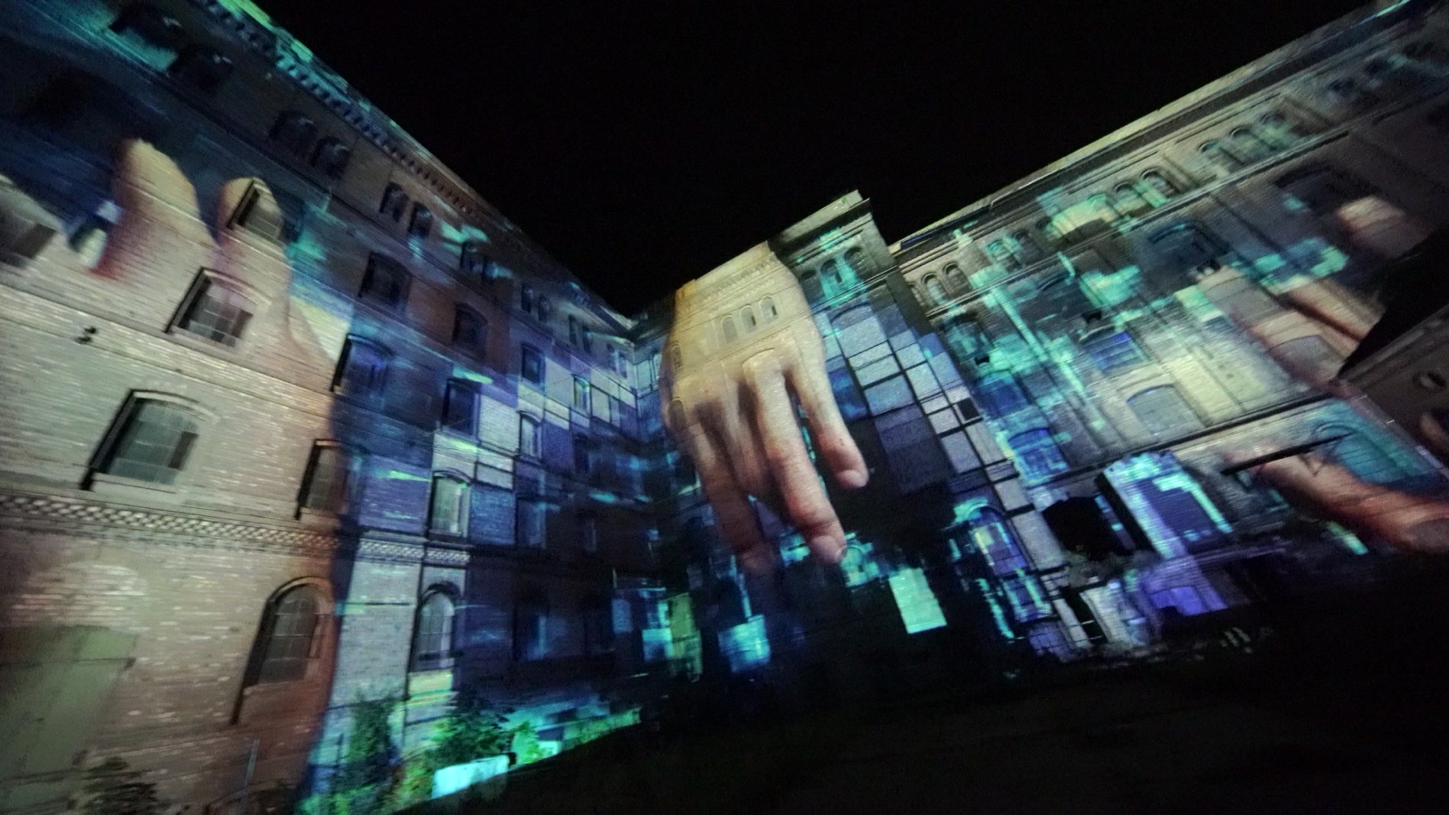 Two brick wings of the Löhnberger Mühle in Lahnstein with giant hands and blue pixel blocks projection-mapped onto the façade, rheinleuchten 2021
