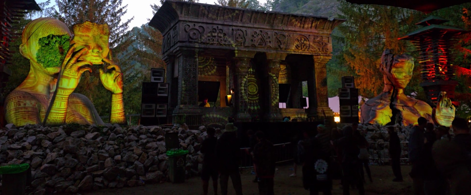 The Swamp stage at MO:DEM Festival with its giant figure sculptures and temple façade mapped in yellow and green light, the crowd in front
