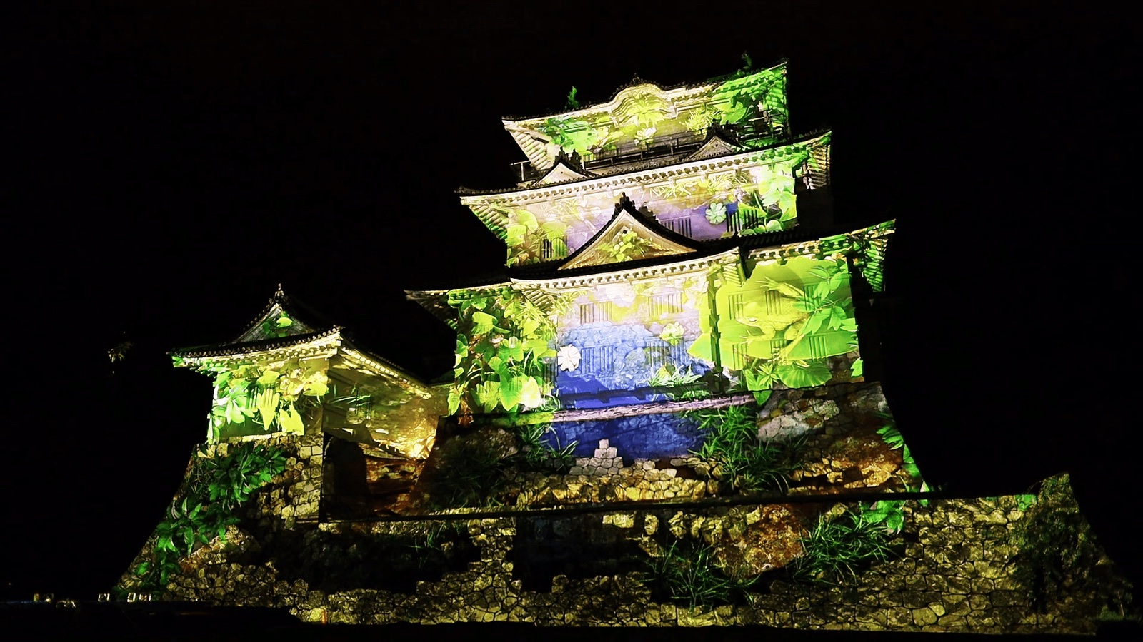 The white-walled keep of Odawara Castle in Japan glowing in green and gold from a 3D projection mapping at night