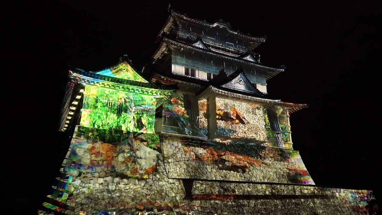 The white-walled keep of Odawara Castle in Japan glowing in green and gold from a 3D projection mapping at night