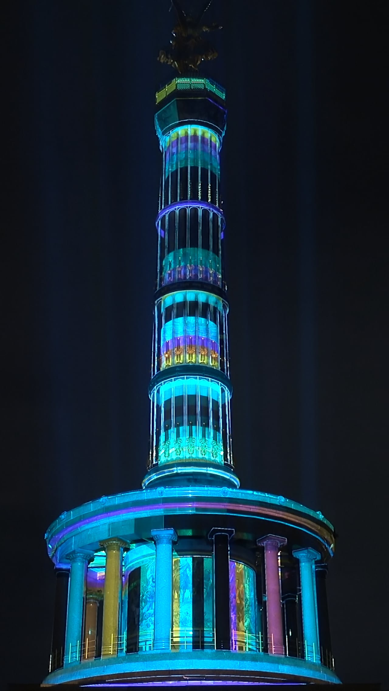 The Berlin Victory Column illuminated in turquoise and blue by a 3D projection mapping at night, filmed in vertical format