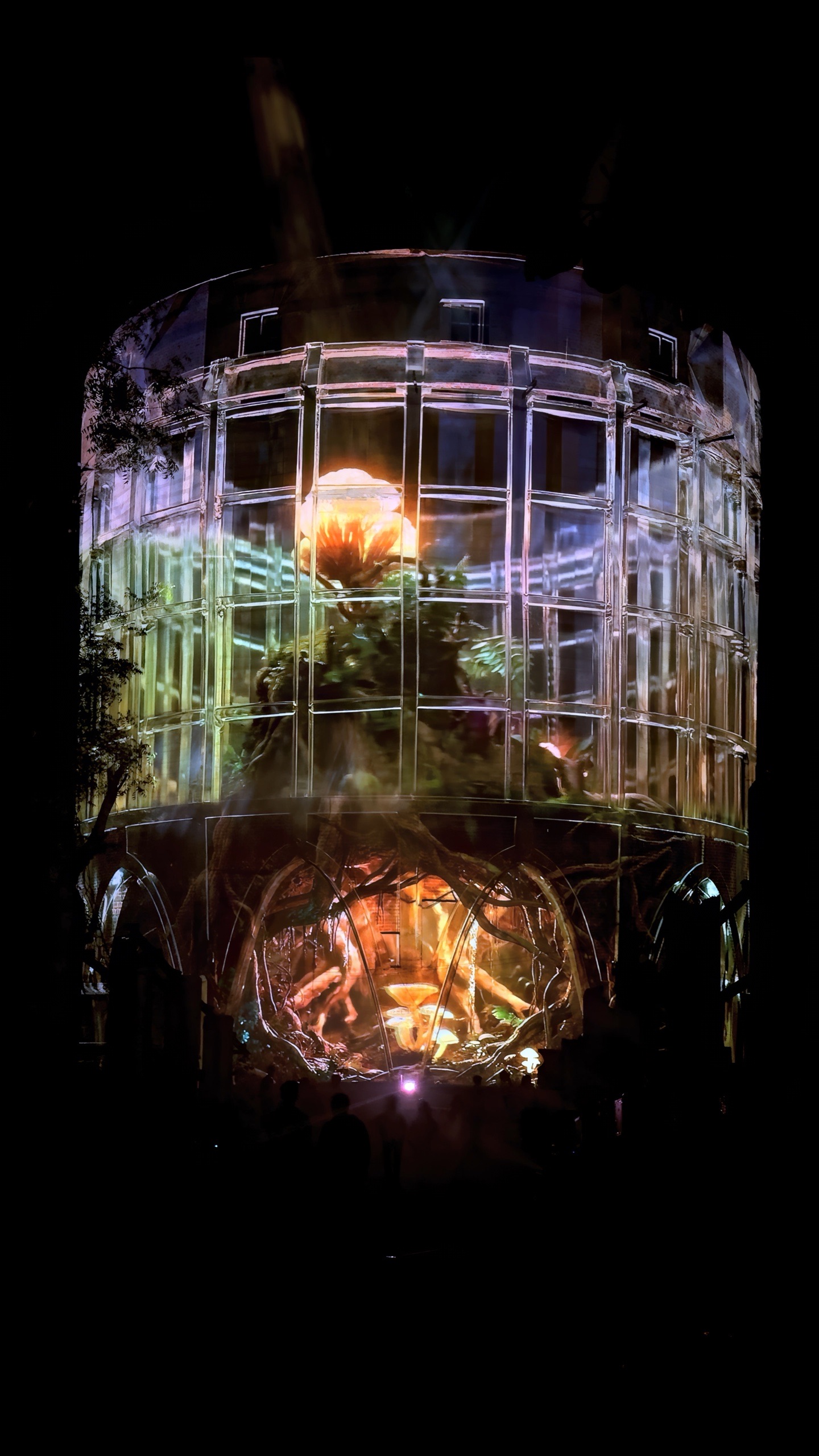 The concrete silo of the Alembic Glass Factory in Bengaluru rendered as a transparent lattice by projection, with an amber interior glowing inside and holographic fog around it